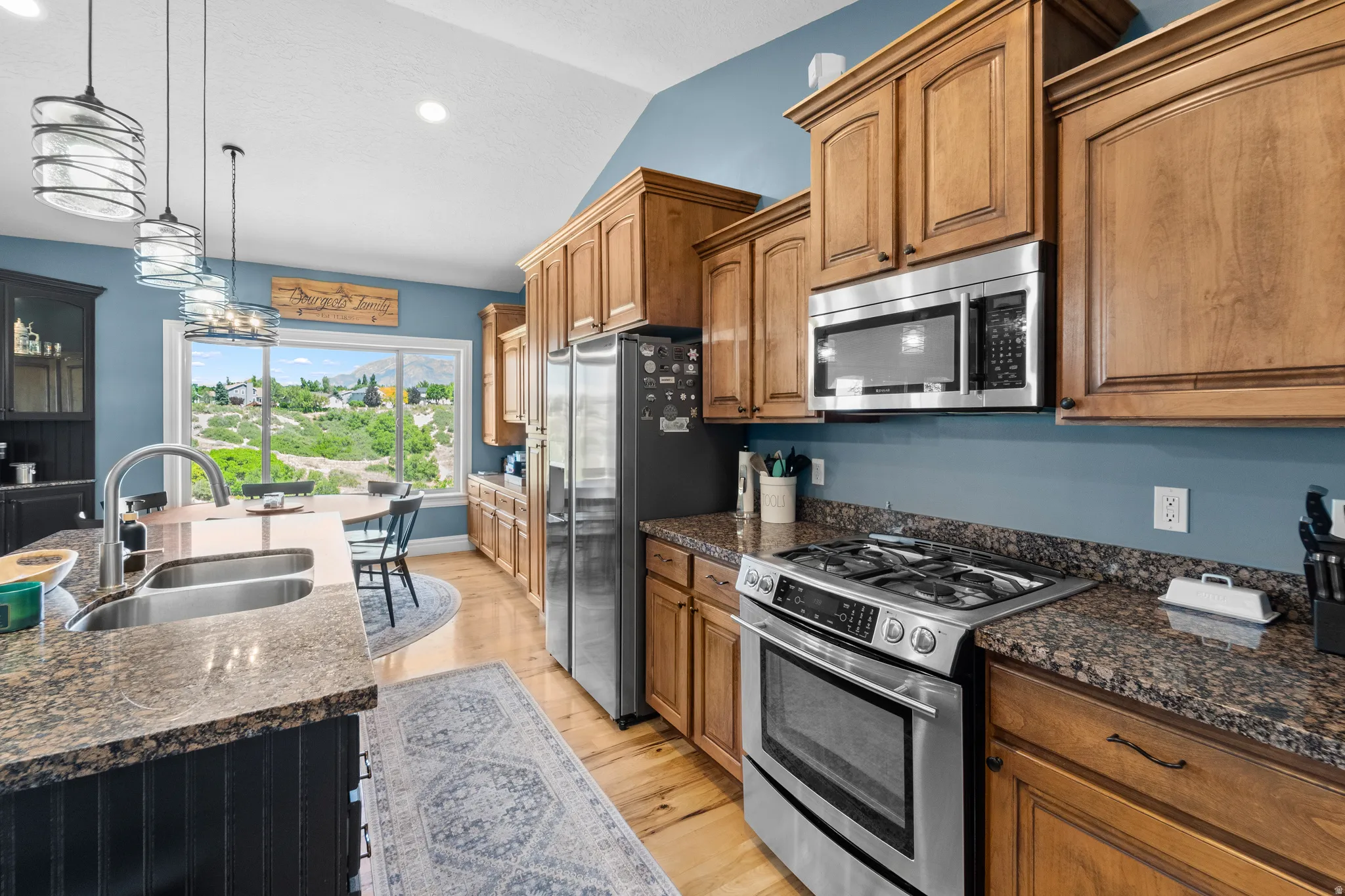 Kitchen featuring wood cabinetry, stainless steel appliances, granite countertops, and light wood-finish flooring