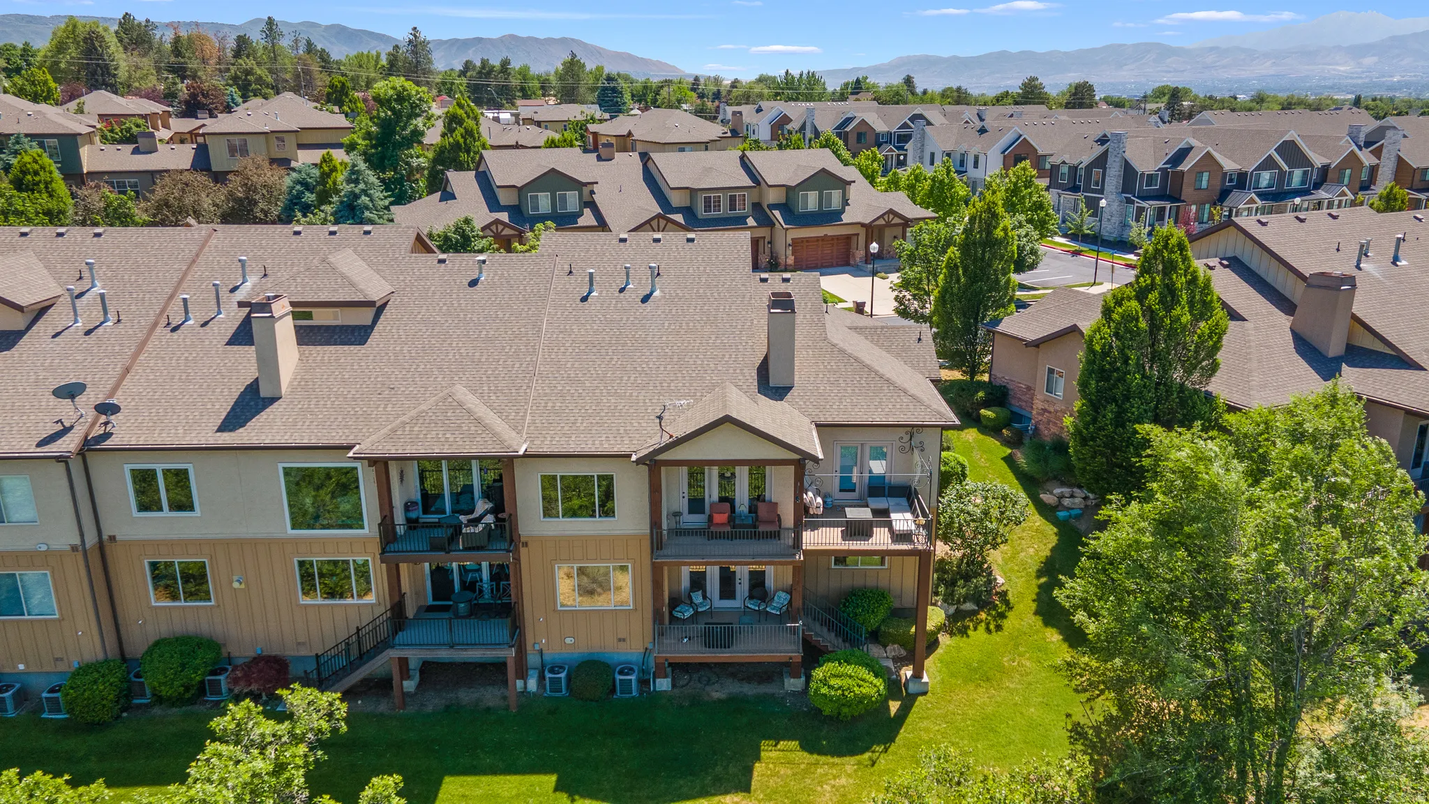 Multi-level property featuring a neutral-toned exterior with multiple windows and balconies, set against a backdrop of distant mountains