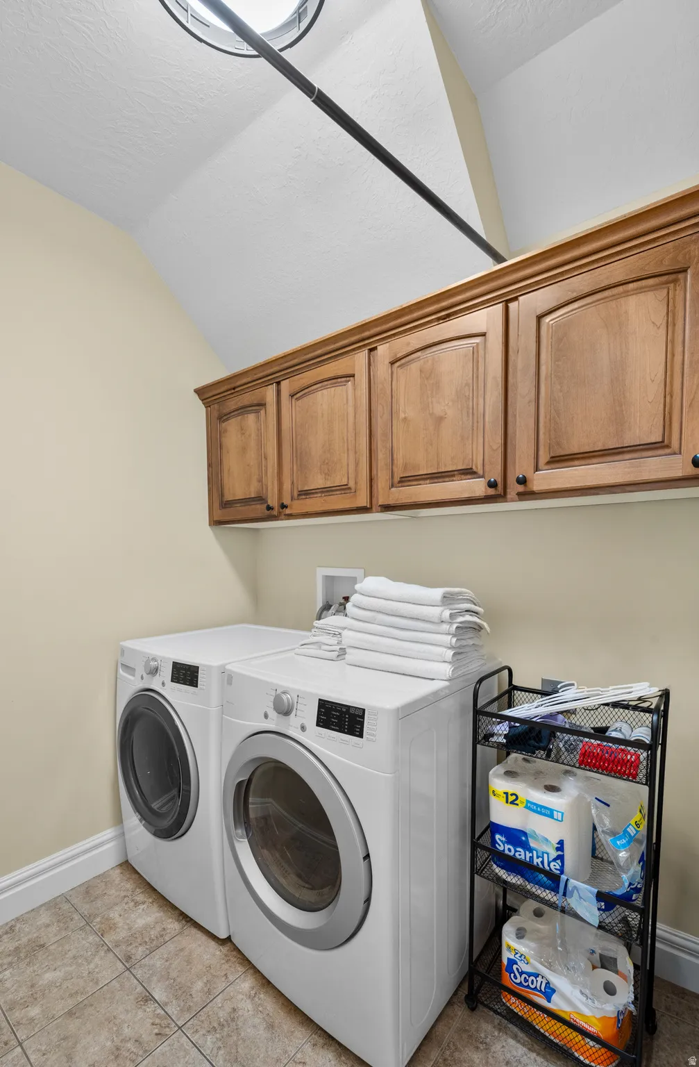 Functional laundry area featuring upper wood cabinetry, tile flooring, and a skylight