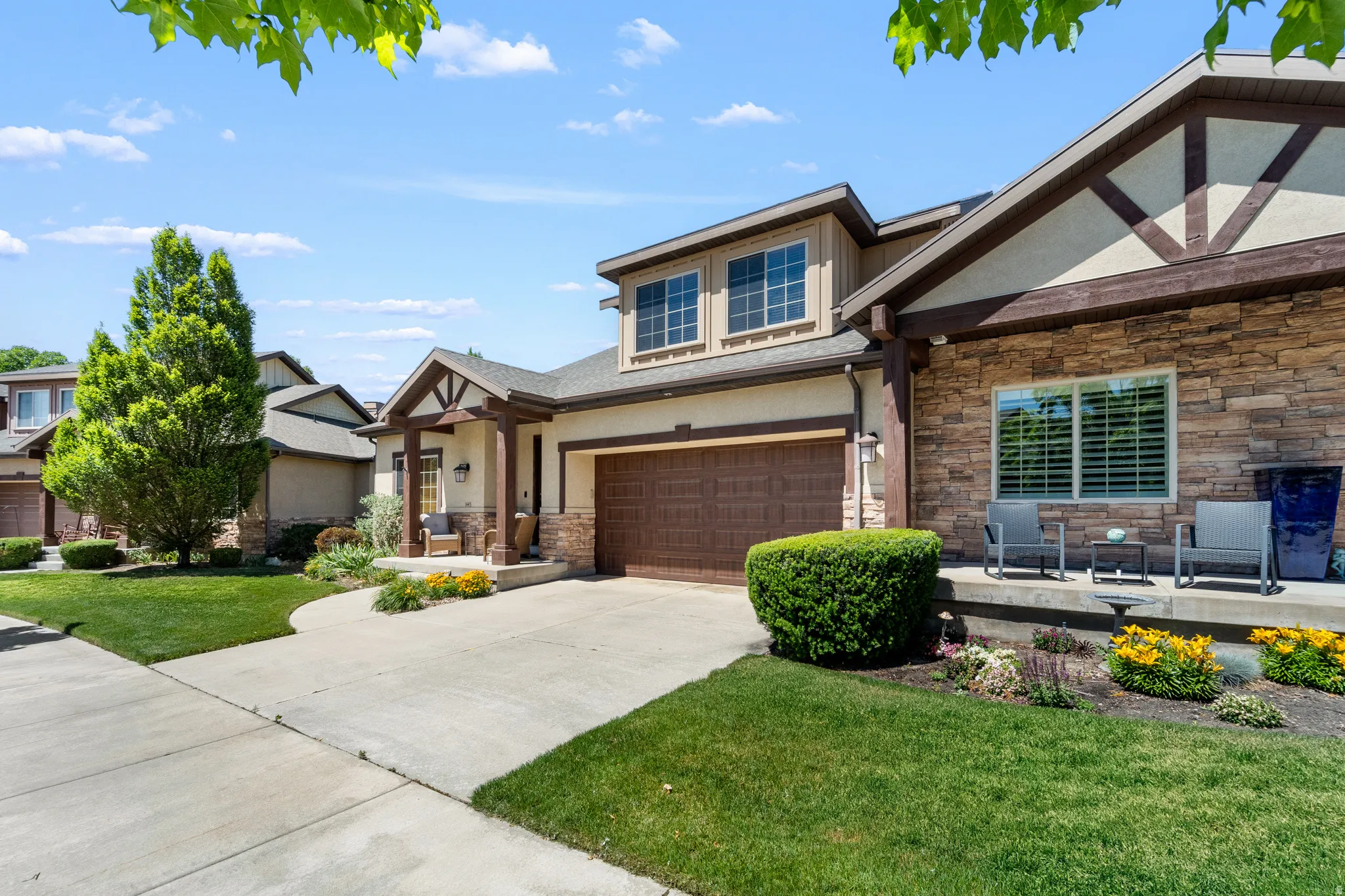 Exterior featuring stone accents, stucco siding, a wood-finish garage door, and a covered front porch