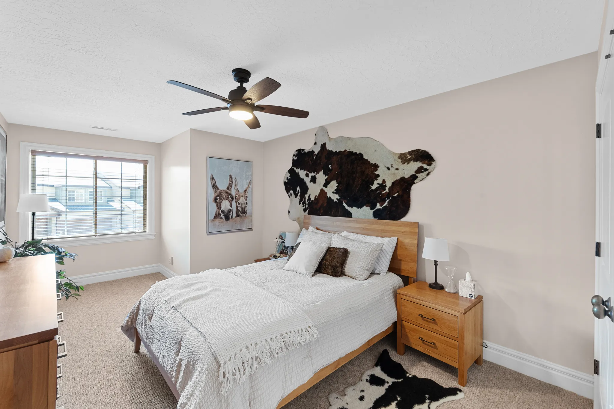 Carpeted bedroom featuring a ceiling fan with integrated lighting, a large window with white trim, and light beige wall paint