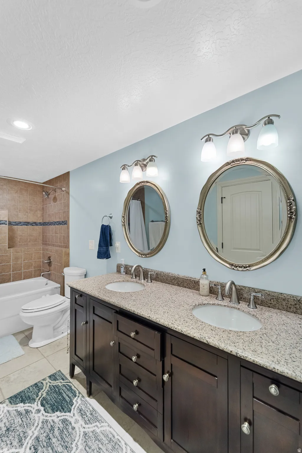 Bathroom with a double vanity featuring a light-colored speckled countertop, two oval undermount sinks, and dark wood-finish cabinetry