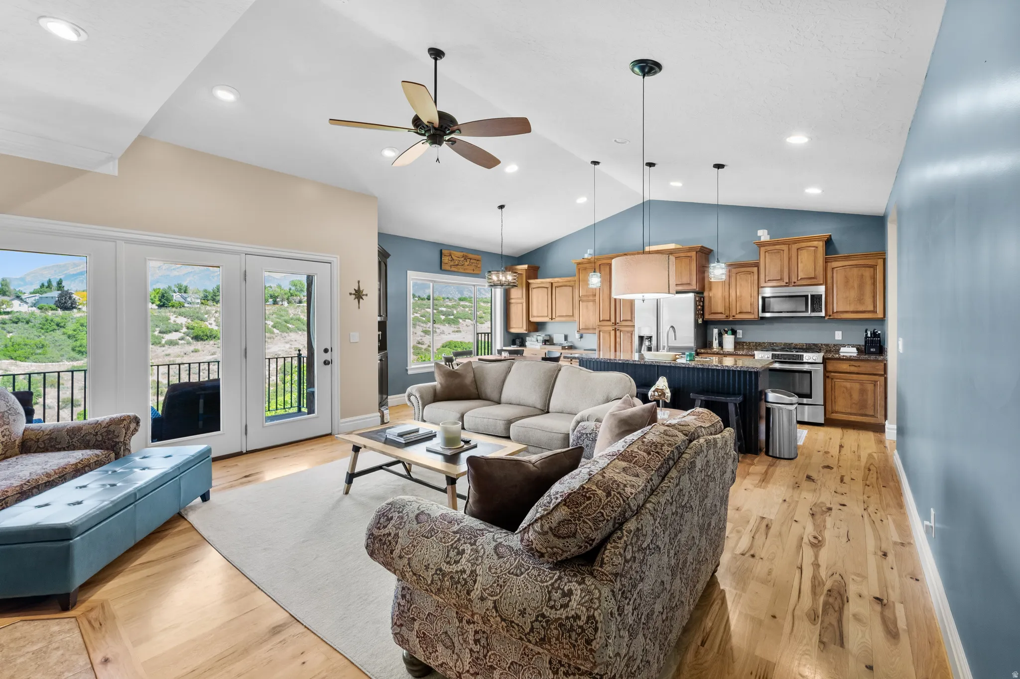 Open-concept living space featuring wood-finish flooring, vaulted ceilings with recessed lighting, and a kitchen with wood cabinetry and stainless steel appliances