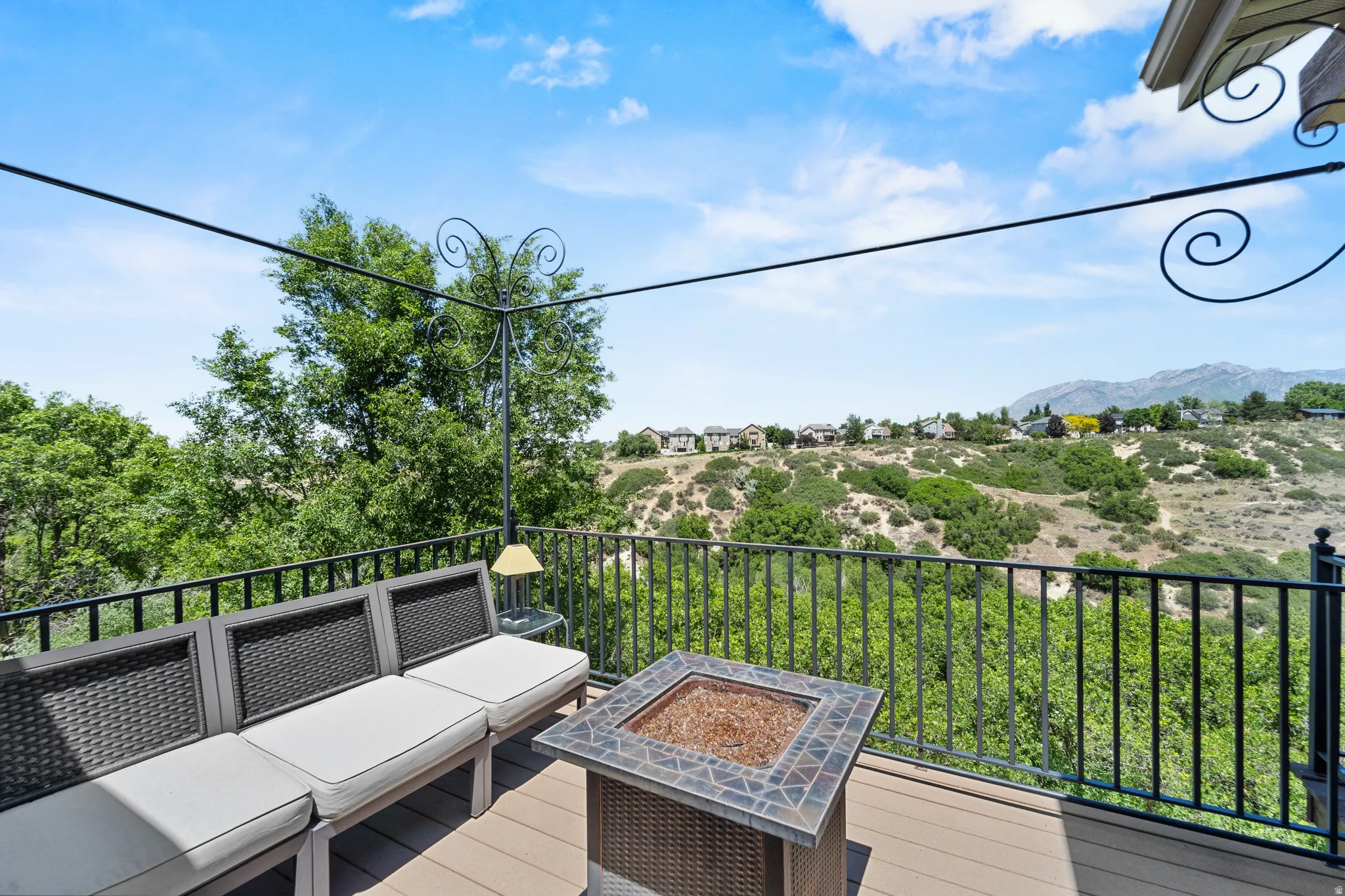 Spacious outdoor deck featuring wood-finish flooring, black metal railings, and a built-in fire pit with a mosaic tile surround