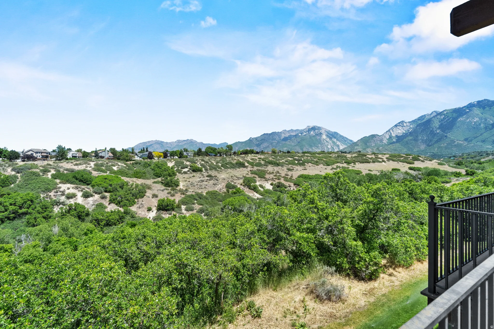 Expansive mountainous landscape featuring distant peaks, verdant tree coverage, and a clear blue sky