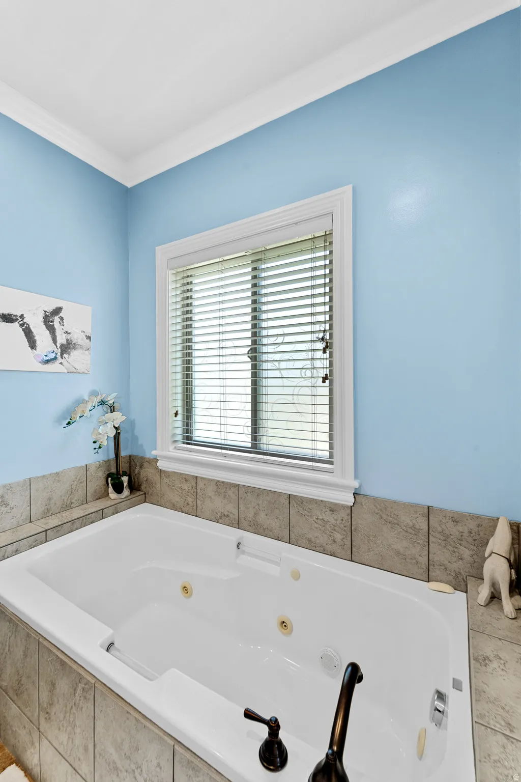 Soaking tub with bronze-finish fixtures, surrounded by tile-clad decking and a window with blinds