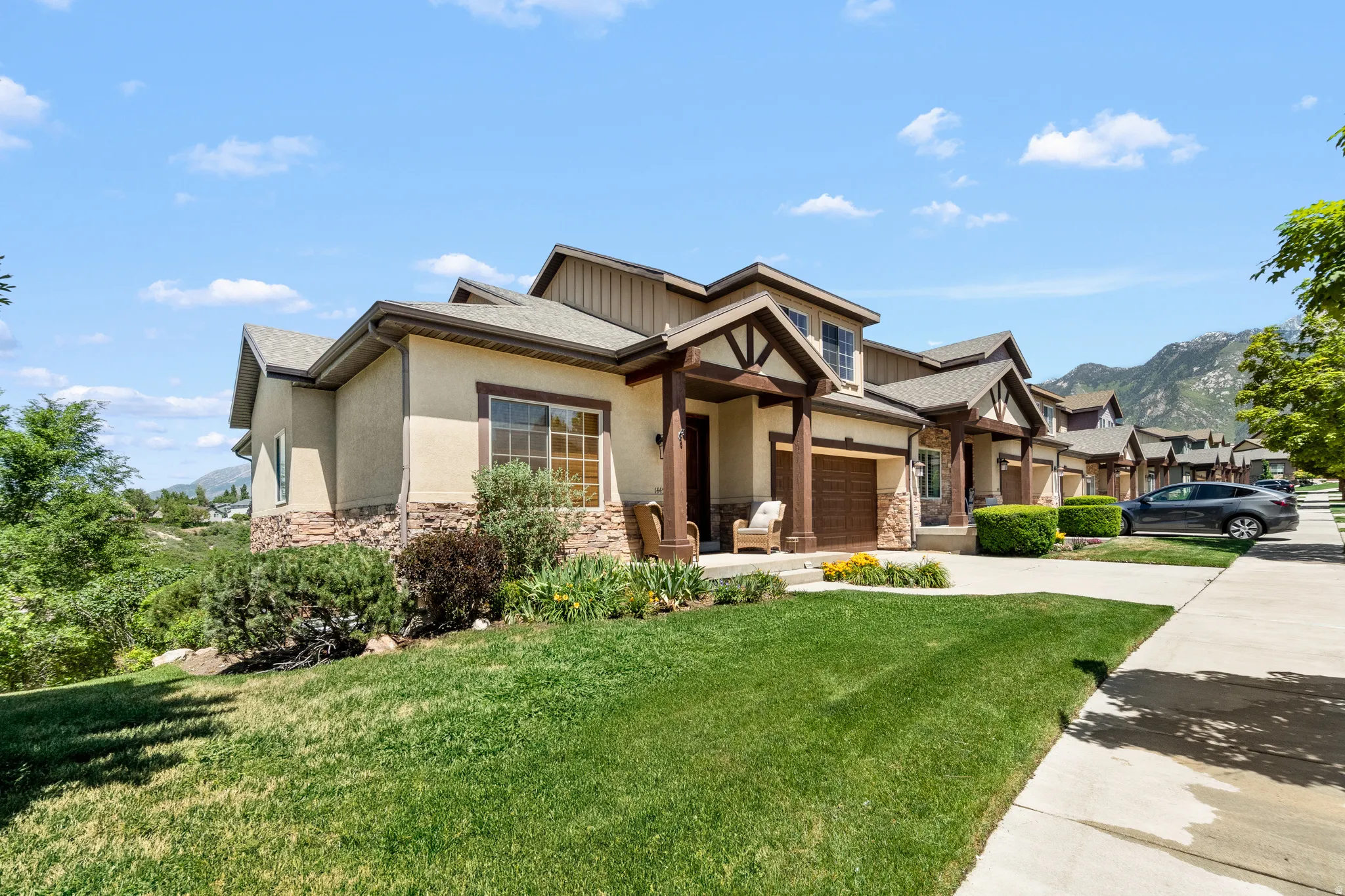 Exterior featuring stone and stucco finishes, a covered porch entry, an attached garage, and landscaping with mature plantings