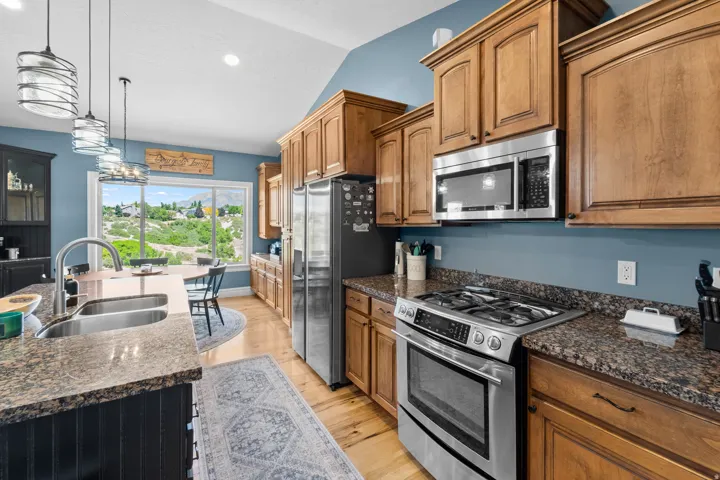 Kitchen featuring wood cabinetry, stainless steel appliances, granite countertops, and light wood-finish flooring