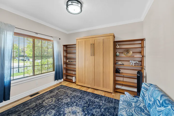 Room featuring light wood-finish flooring, a large window with horizontal blinds, built-in wooden shelving, a built-in wall bed, and crown molding