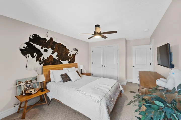 Carpeted bedroom featuring a ceiling fan with integrated lighting, a wooden headboard, and dual white paneled doors