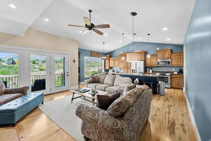 Open-concept living space featuring wood-finish flooring, vaulted ceilings with recessed lighting, and a kitchen with wood cabinetry and stainless steel appliances