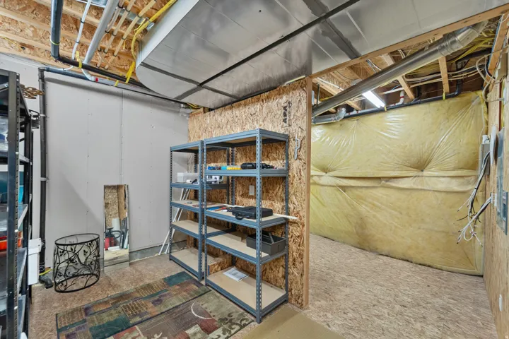 Unfinished basement area featuring exposed ceiling joists, visible ductwork, and partial insulation