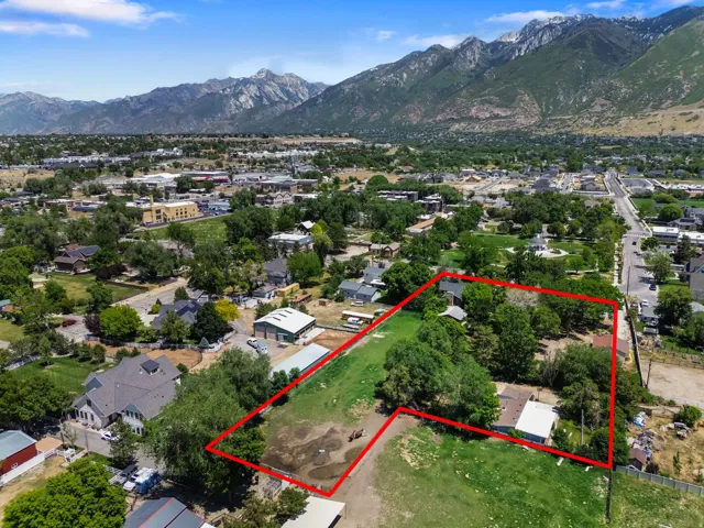 Aerial perspective showcasing a large parcel with mature trees and a residential structure, framed by distant mountains