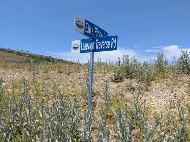 Road sign indicating "Elks Ridge Rd" and "Lakeview Traverse Rd" on a hillside with sparse vegetation under a clear blue sky