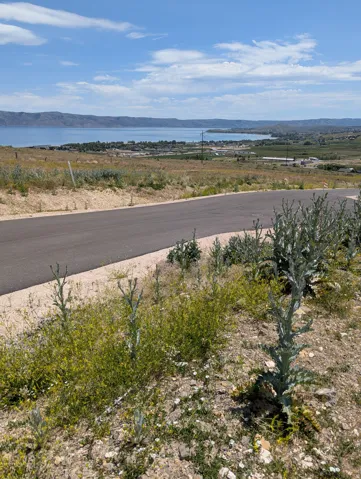 Paved road with a natural landscape, offering expansive water and distant mountain scenery under a partly cloudy sky
