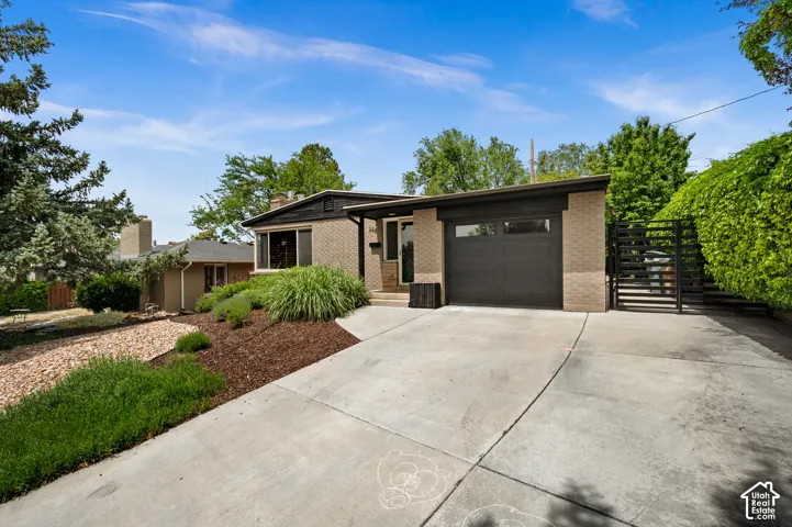 Brick exterior featuring a dark-toned garage door, concrete driveway, and established landscaping