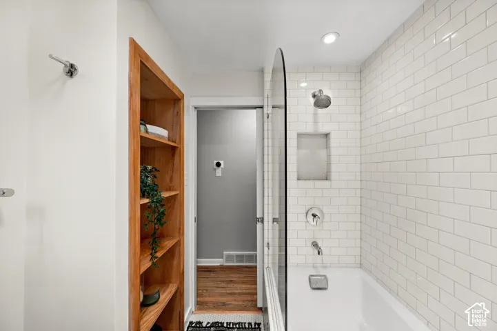 Tiled shower/tub combination with subway tile surround, recessed niche, and clear glass partition