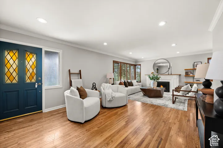 Living room featuring wood-finish flooring, recessed lighting, and a white fireplace with a dark surround