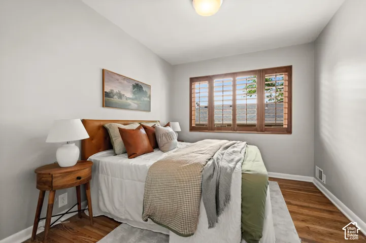 Bedroom featuring wood-finish flooring, light gray wall paint, and a window with custom wood plantation shutters