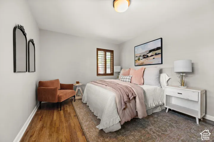Bedroom featuring hardwood flooring, light gray walls, and a window with wood plantation shutters