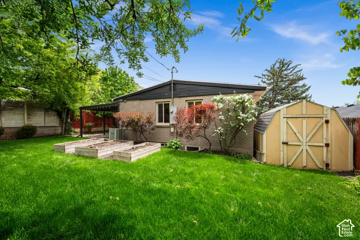 Expansive green lawn featuring three raised garden beds, a storage shed, and a covered patio area