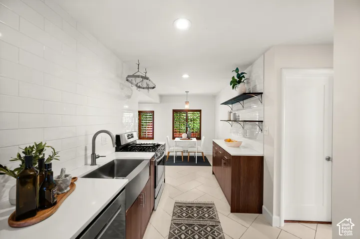 Contemporary kitchen featuring white subway tile backsplash, white countertops, stainless steel appliances, and wood-finish cabinetry