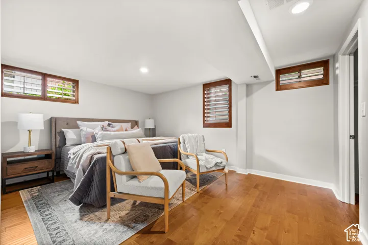 Spacious bedroom featuring wood-finish flooring, recessed lighting, and wall-mounted windows with wood shutters