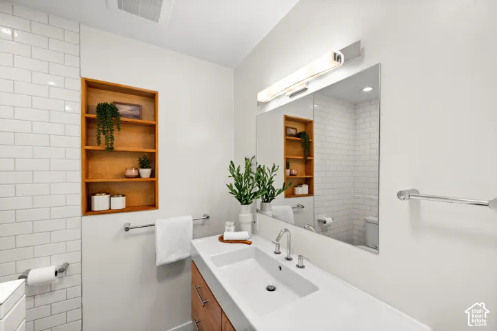 Contemporary bathroom featuring a wide integrated sink, a rectangular mirror with overhead lighting, a built-in wooden shelving unit, and subway tile accents