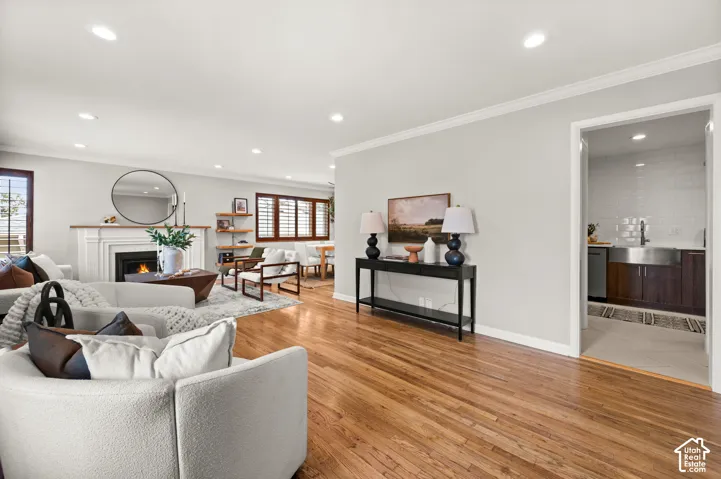 Spacious living area featuring polished wood-finish flooring, a white mantel fireplace, recessed lighting, and crown molding