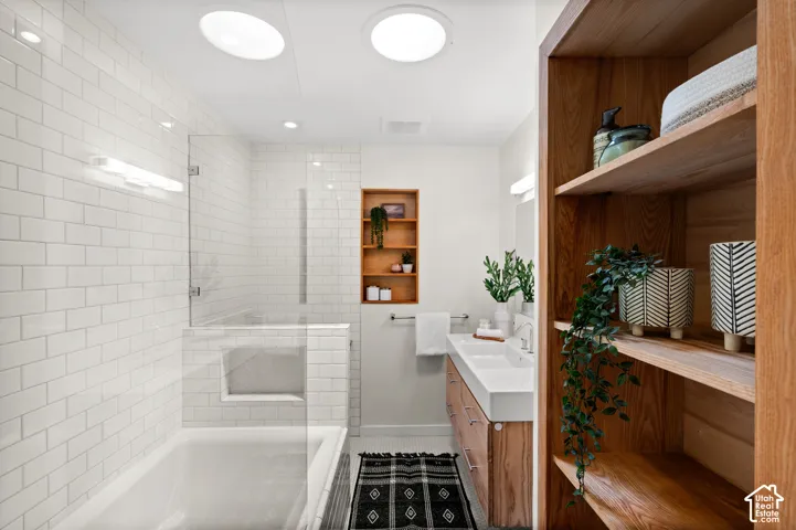Bathroom featuring a tub and shower combination with glass enclosure, white subway tile surround, and recessed shelving