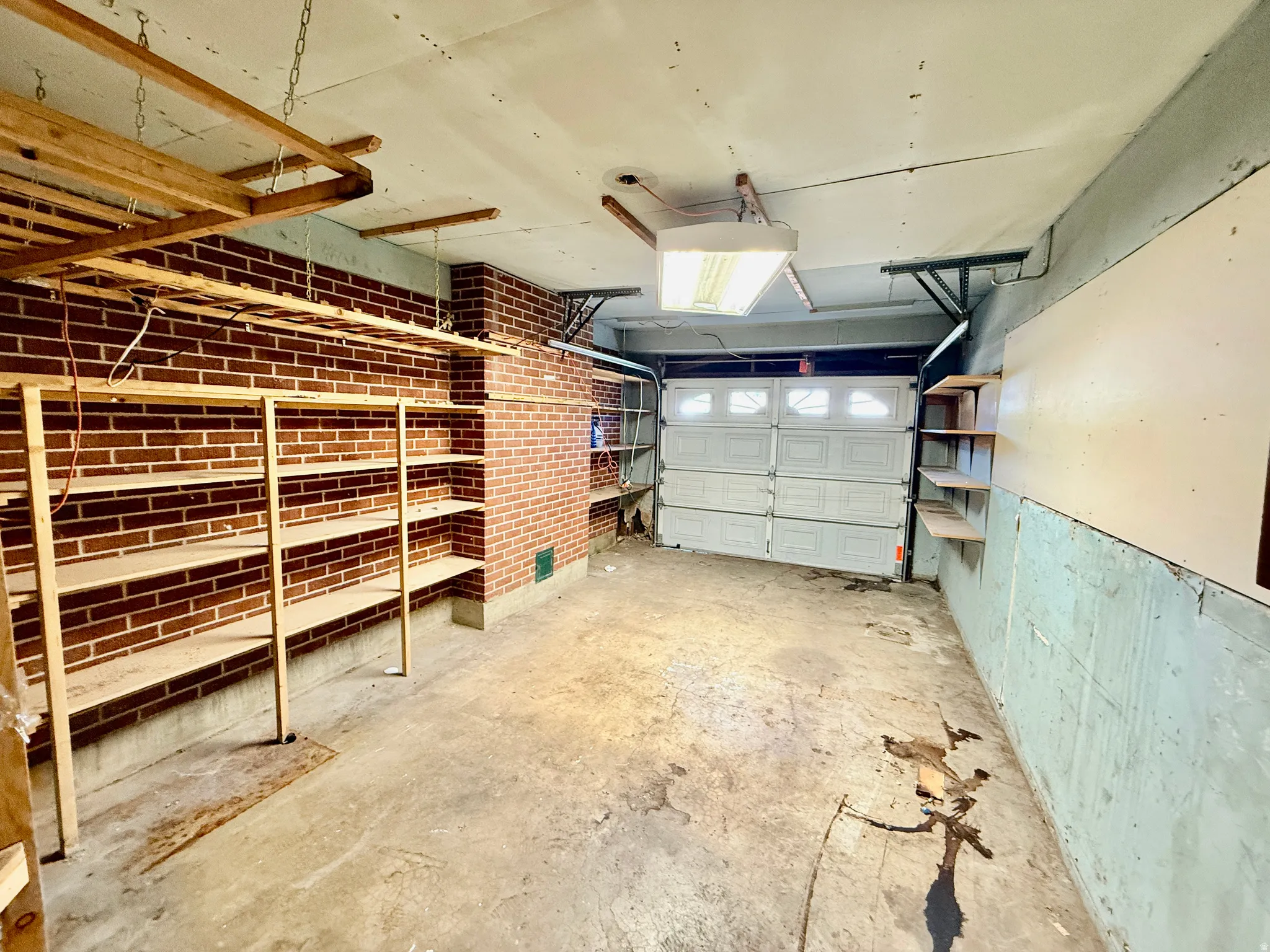 Garage interior featuring a sectional garage door, exposed brick wall, concrete flooring, and built-in shelving units