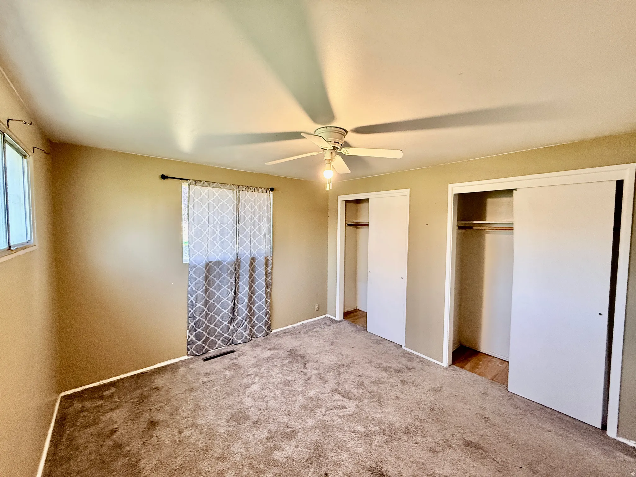 Carpeted room featuring a ceiling fan with integrated lighting, two windows, and two sliding door closets with interior shelving and hanging rods