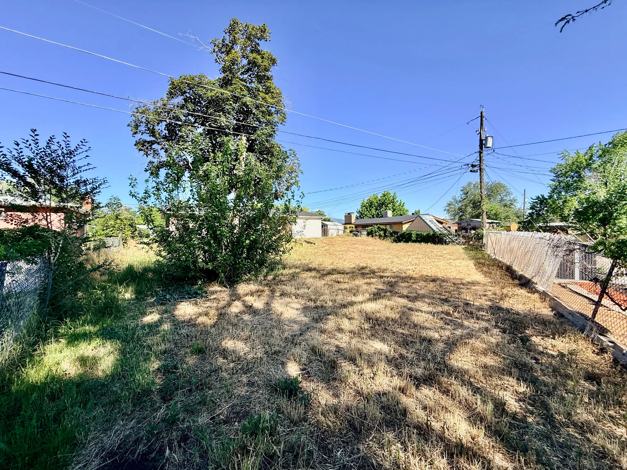 Expansive lot featuring mature trees, partial fencing, and clear blue skies