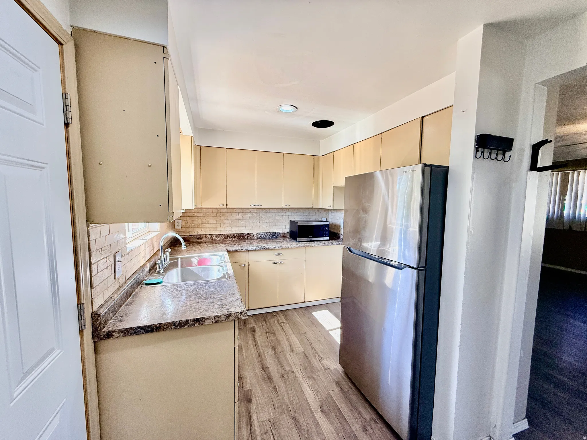 Kitchen featuring wood-finish flooring, light-toned cabinetry, stainless steel refrigerator, patterned countertops, and a tiled backsplash