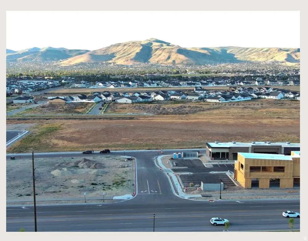 Expansive mountain backdrop with a developing residential community, new commercial construction, and a paved street