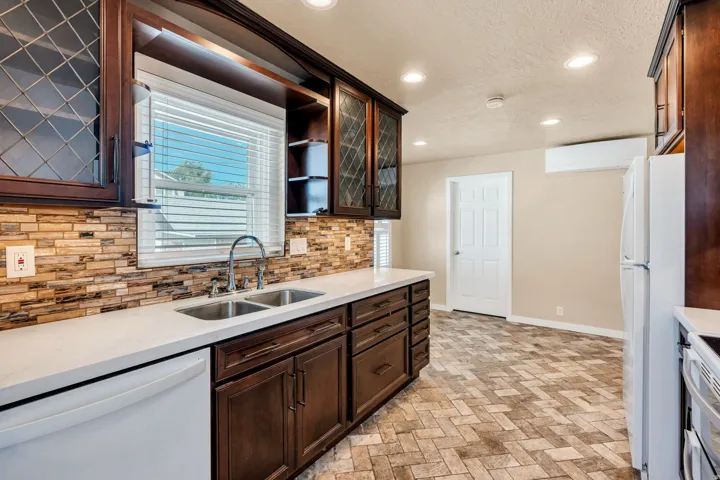 Kitchen featuring dark wood-finish cabinetry with glass-front uppers, light countertops, and a textured tile backsplash