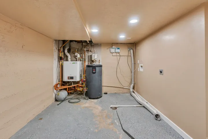Utility area featuring a water heater, boiler, visible copper piping, and a concrete-finish floor