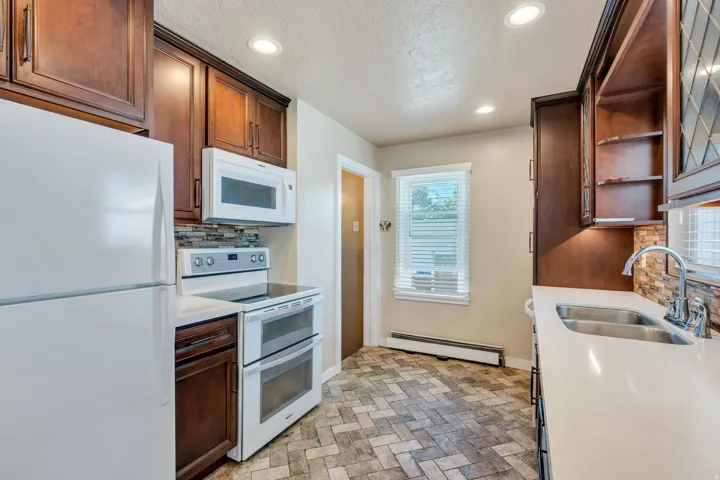 Kitchen featuring rich wood cabinetry, stone-look tile flooring in a herringbone pattern, white countertops, and a double basin stainless steel sink with a gooseneck faucet