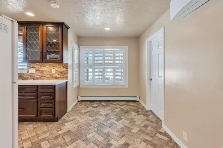 Kitchen area featuring herringbone-patterned flooring, dark wood cabinetry with glass-front uppers, a light-toned countertop, and a mosaic tile backsplash