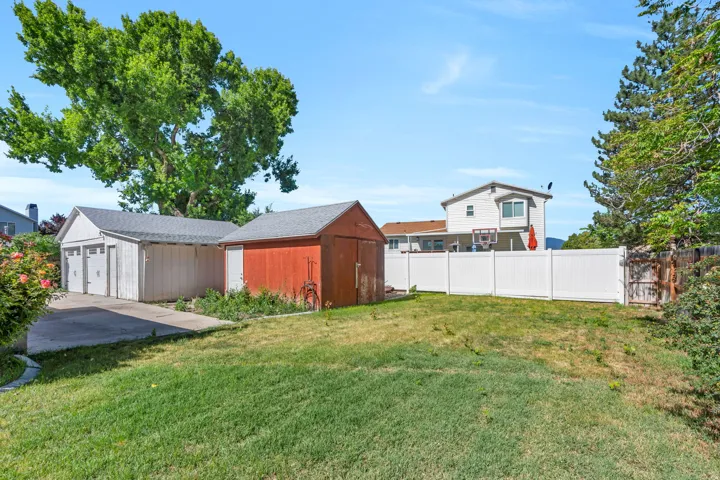 Expansive backyard featuring a manicured lawn, a detached two-car garage with individual doors, a separate red storage shed, a white privacy fence, and mature trees