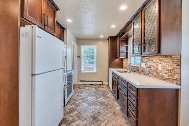 Kitchen featuring dark wood cabinetry, white countertops, tile backsplash, stainless steel sink, and patterned floor tiles