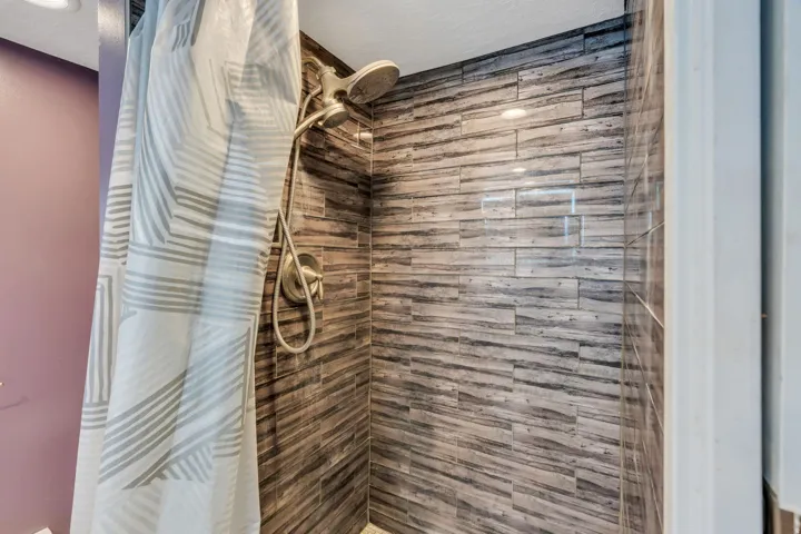 Shower stall with horizontal wood-look tile, recessed lighting, and a brushed nickel showerhead with a handheld sprayer
