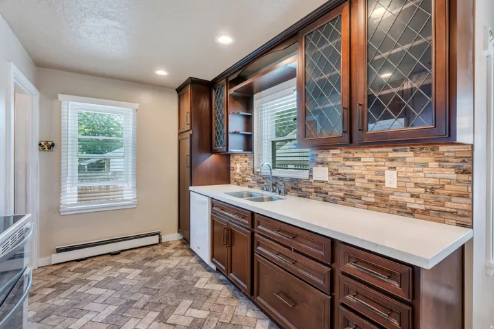 Kitchen featuring wood cabinetry with leaded glass accents, light-toned countertops, a multi-toned tile backsplash, and recessed lighting