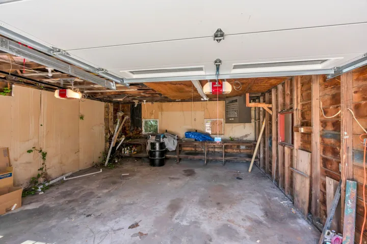 Attached garage with an overhead door, exposed wood framing, and a concrete floor