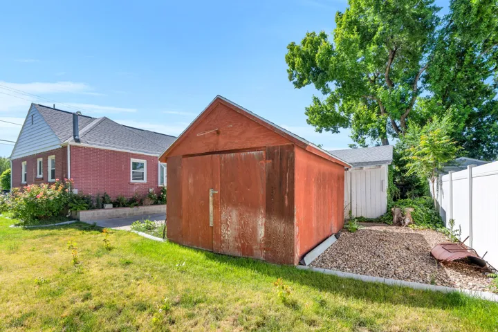 Red-painted outbuilding with double doors, featuring a gravel bed and adjacent grassed area