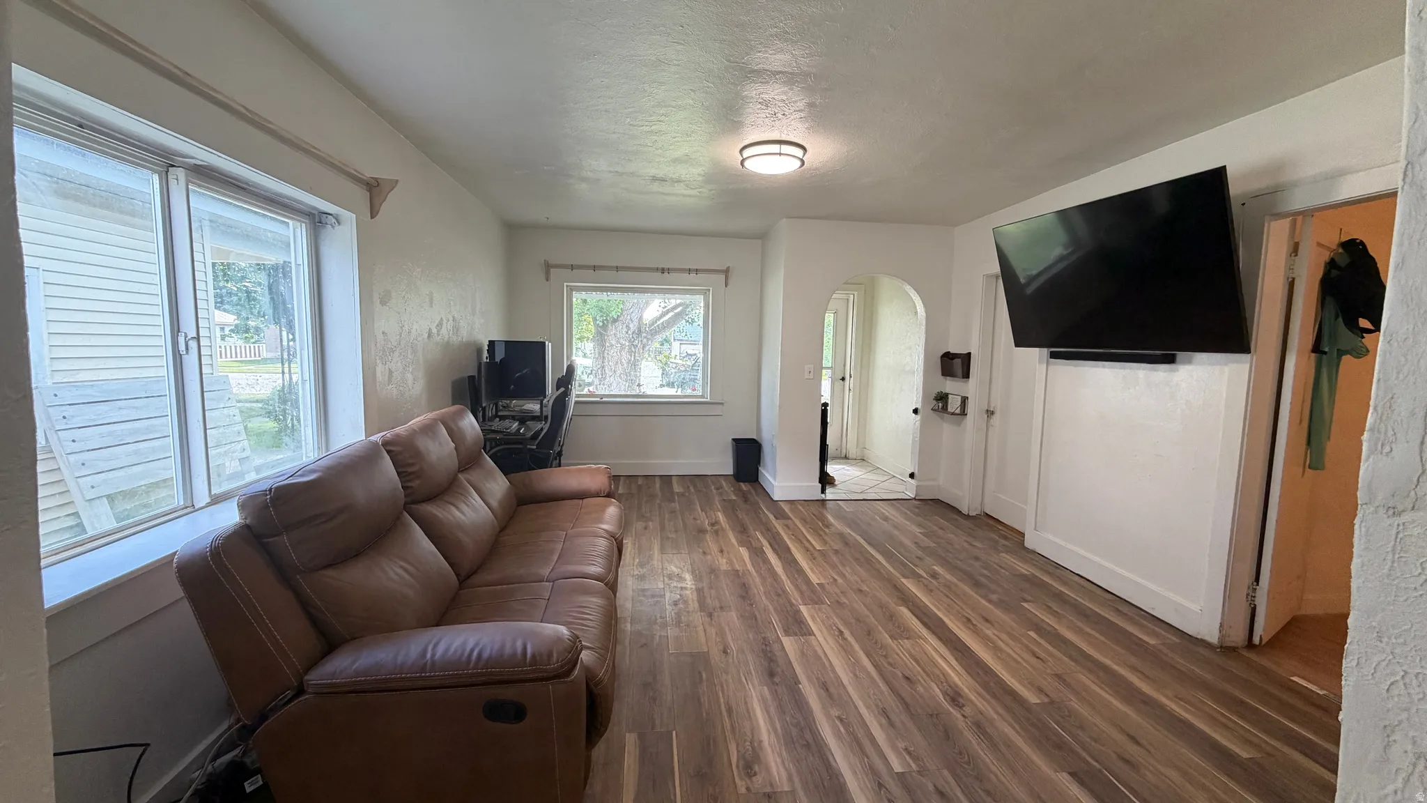 Living area featuring wood-finish flooring, white walls, and an arched doorway