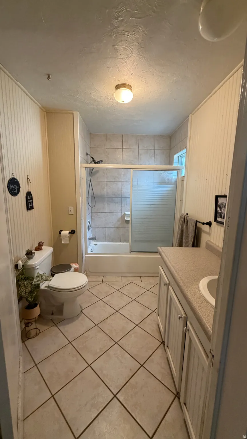 Bathroom featuring a tiled shower/tub combination with a sliding glass enclosure, a single vanity with storage, a toilet, and diagonal tile flooring
