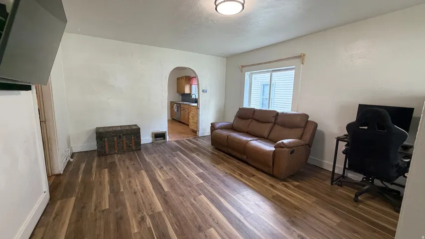 Spacious room featuring wood-finish flooring, white walls, and an arched doorway leading to another area
