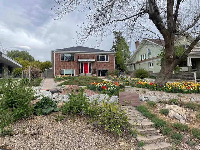 Brick two-story exterior with a distinctive red entry door, front garden, rear garages