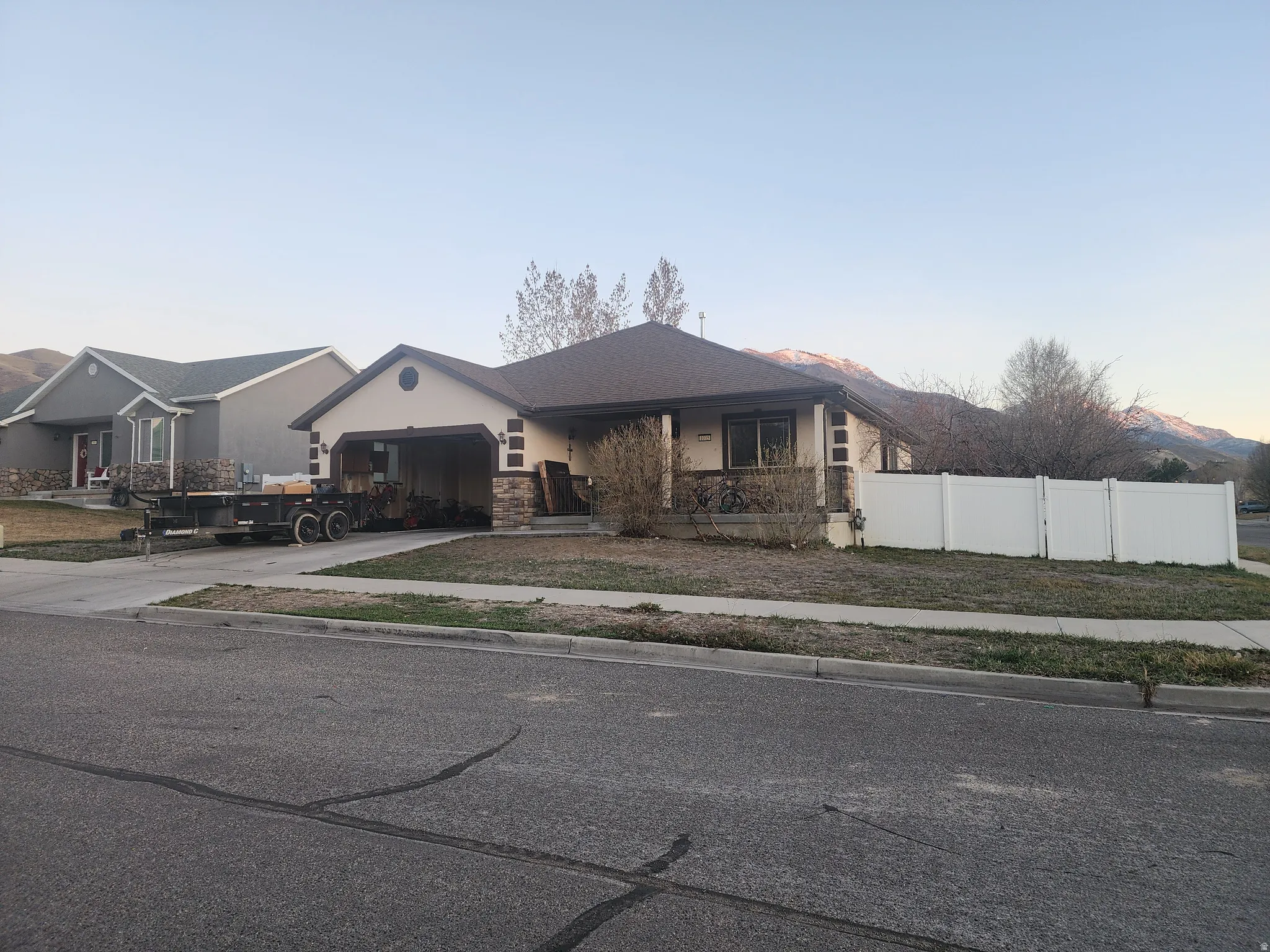 Ranch-style exterior featuring a stone and stucco facade, a two-car garage, and a white vinyl fence